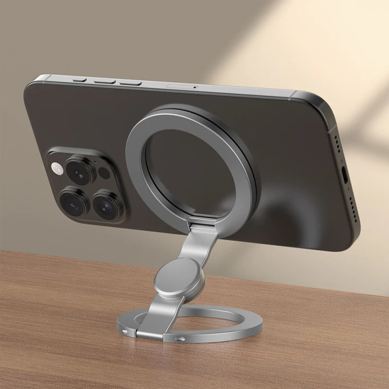 A dark gray foldable dual-sided phone stand with MagSafe compatibility resting on a wooden surface.