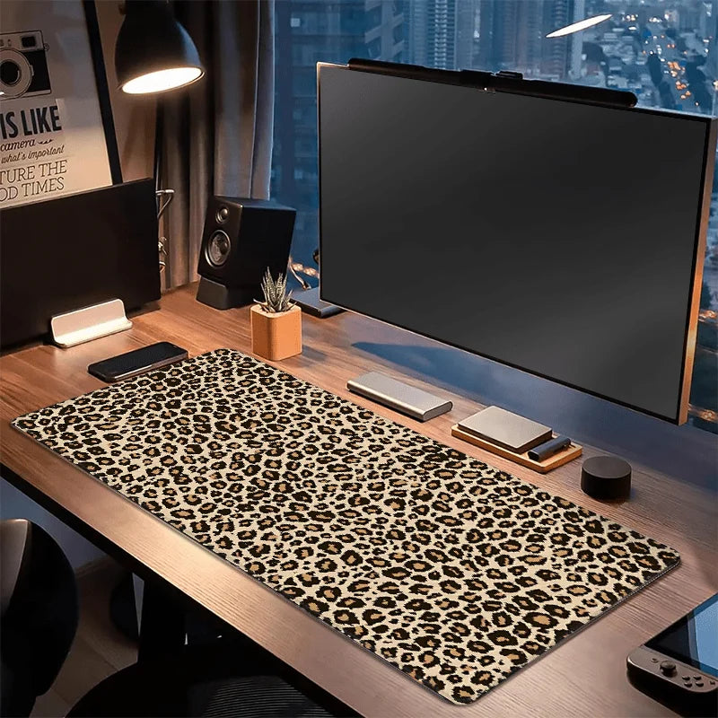 A leopard print XXL gaming mouse pad is displayed on a wooden desk next to a monitor and speakers.