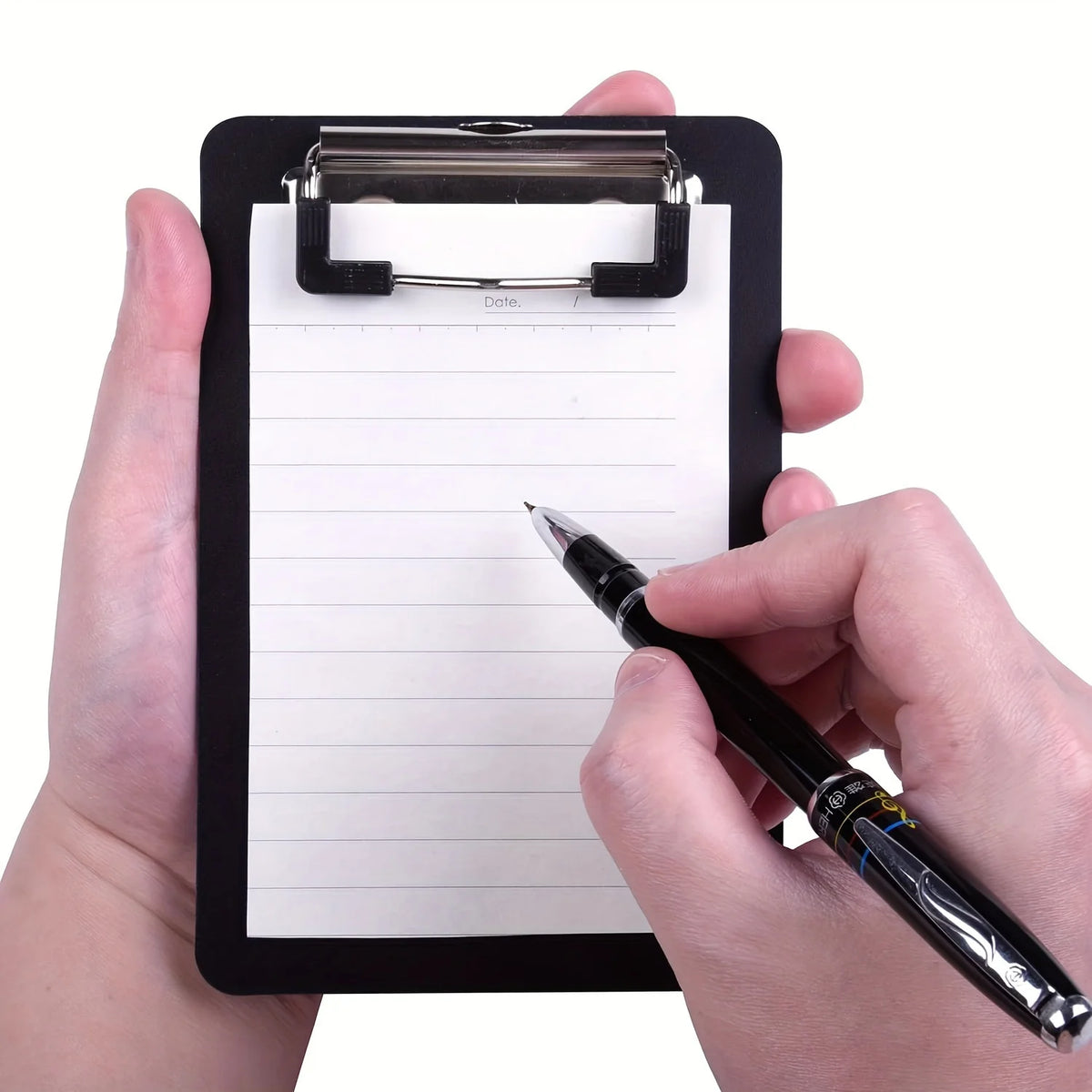 A hand holds a black pocket-sized clipboard with a secure clip, writing on the lined paper with a black pen.