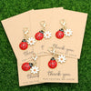 A set of five cute ladybug and daisy keychains are displayed on light brown cards against a green background.