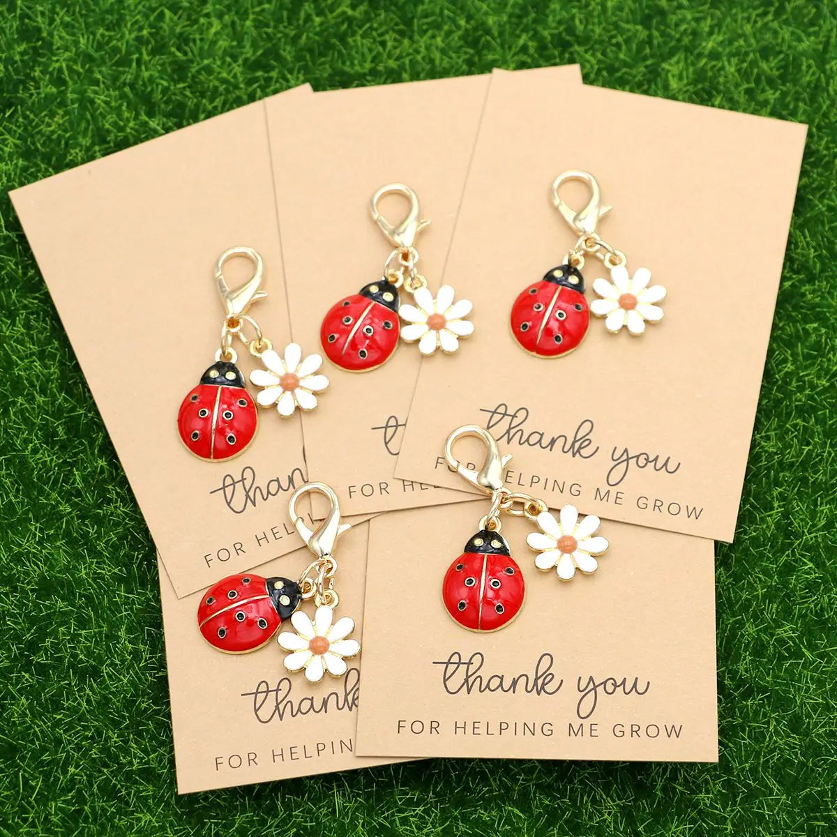 A set of five cute ladybug and daisy keychains are displayed on light brown cards against a green background.