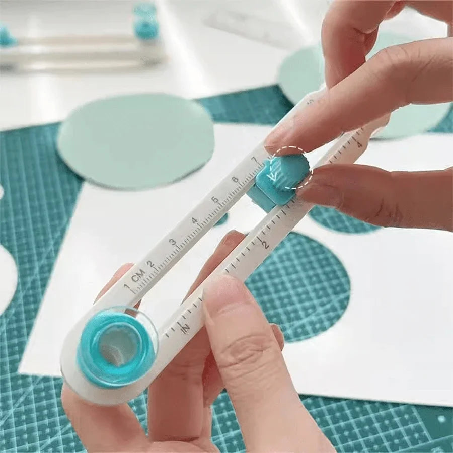 A hand is using a white and blue adjustable circle cutting tool to measure or cut on a green grid surface.