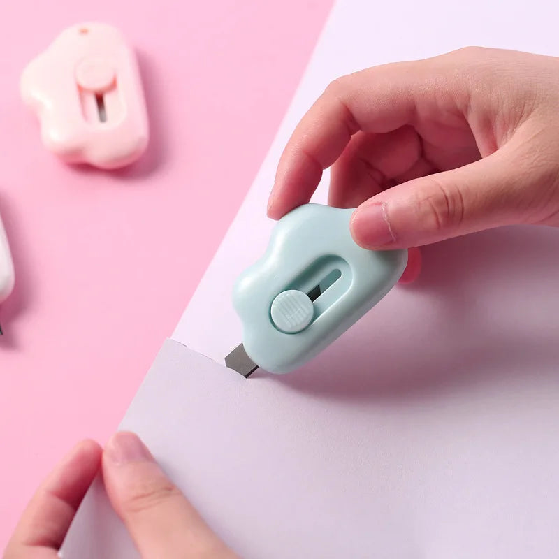 A hand holds a light blue portable utility knife against a pink piece of paper.