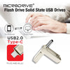 A close-up of a silver plug-and-play flash drive with USB-C and USB 2.0 connectors shown next to a laptop.