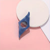 A blue resin thumb book stand is shown resting on a pink surface next to a white circular object.