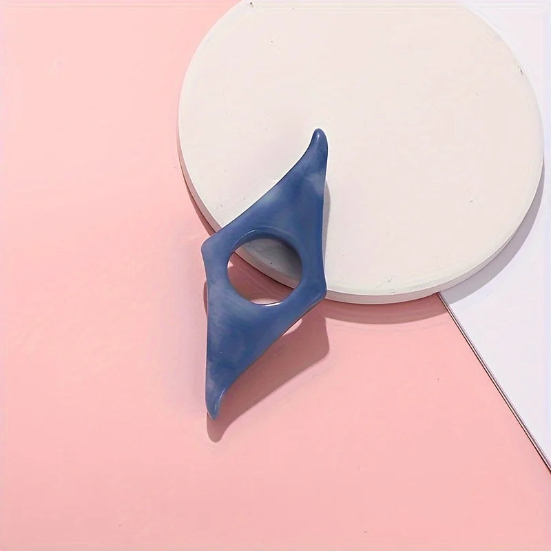 A blue resin thumb book stand is shown resting on a pink surface next to a white circular object.