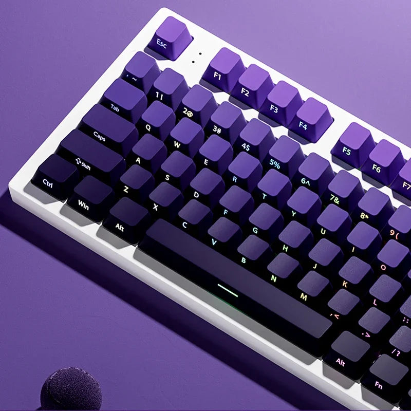 A close-up view of a purple mechanical keyboard with gradient keycaps and RGB lighting, resting on a purple surface.