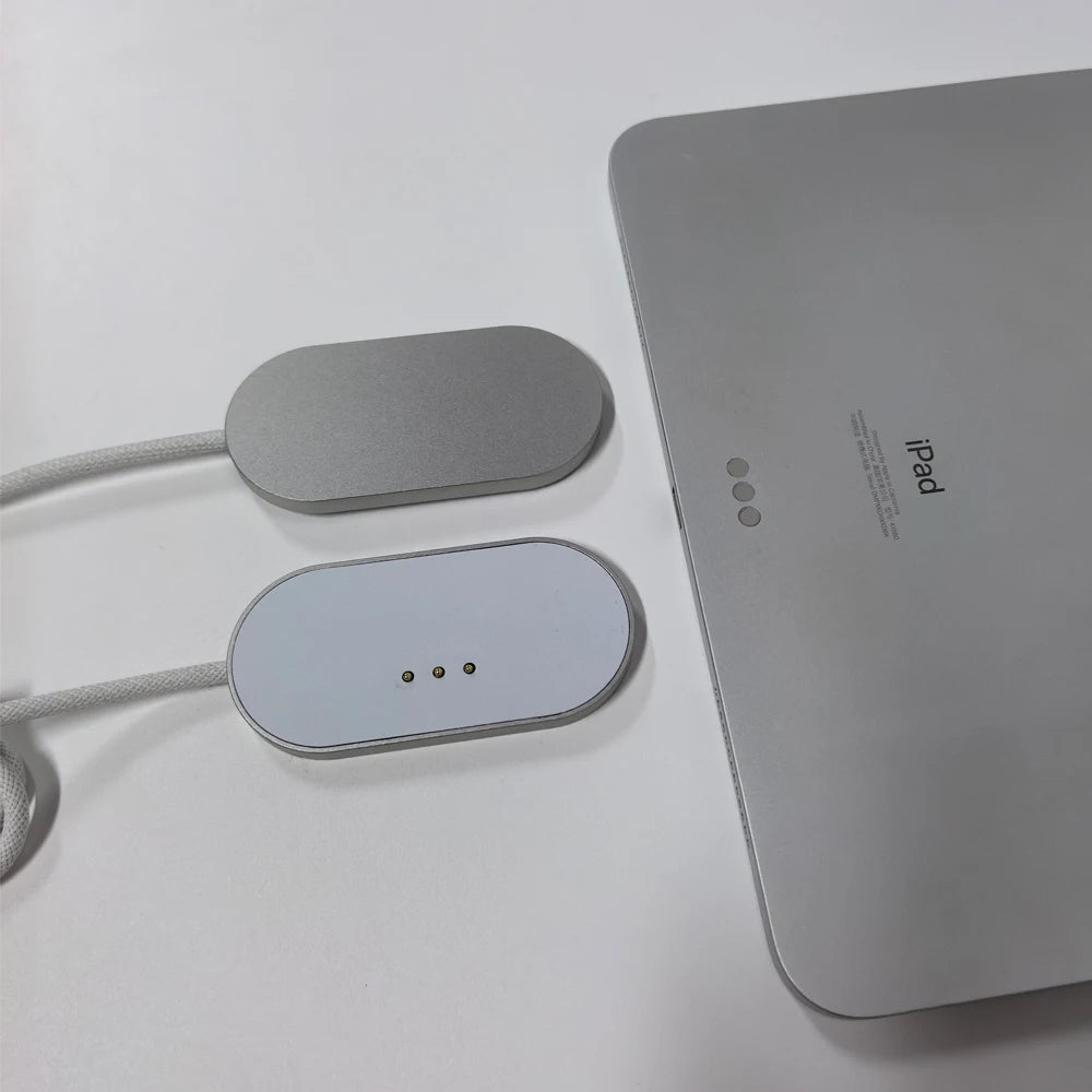 A silver magnetic wireless charging adapter and cable next to an iPad.