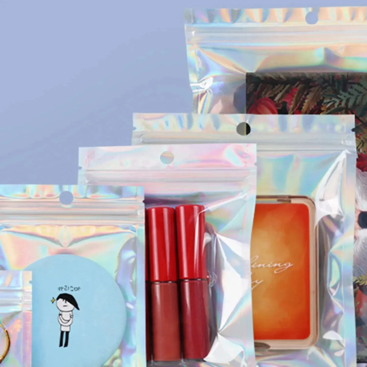 A collection of sealing bags with holographic rainbow patterns, containing red lipsticks and an orange cosmetic product.