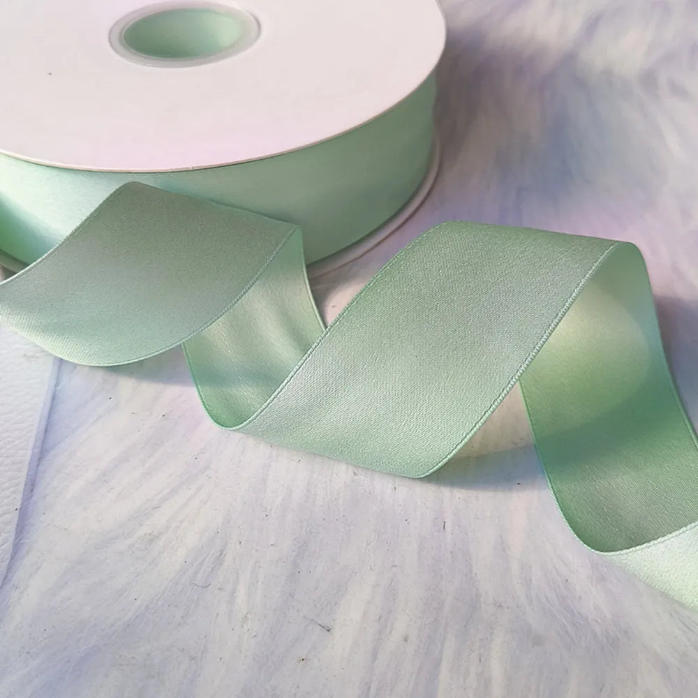 A roll of mint green matte finish satin ribbon is shown unwound, displaying its smooth texture and sheen.
