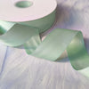 A roll of mint green matte finish satin ribbon is shown unwound, displaying its smooth texture and sheen.