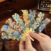 A hand holds a vintage artistic metal bookmark with a gold leaf design and blue floral elements.