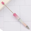 A pink and white DIY beadable pen set with a gold-colored tip resting on a white tiled surface.
