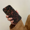 A hand holds an amber leopard print shockproof phone case for an iPhone against a light background.