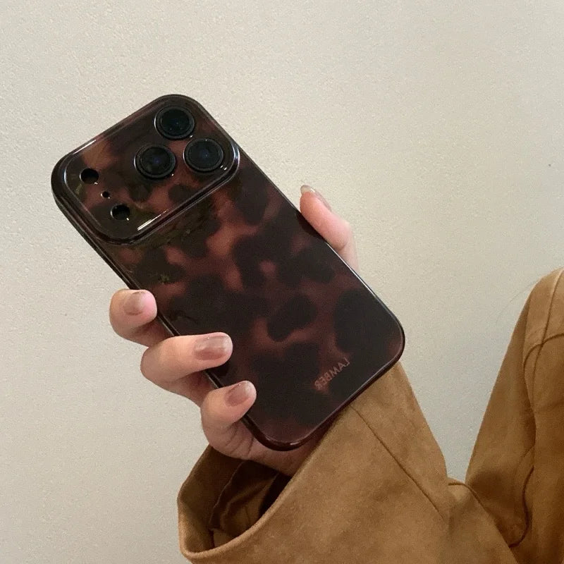 A hand holds an amber leopard print shockproof phone case for an iPhone against a light background.