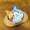 A patchwork cat face coin purse with a zipper featuring various fabric patterns and colors.