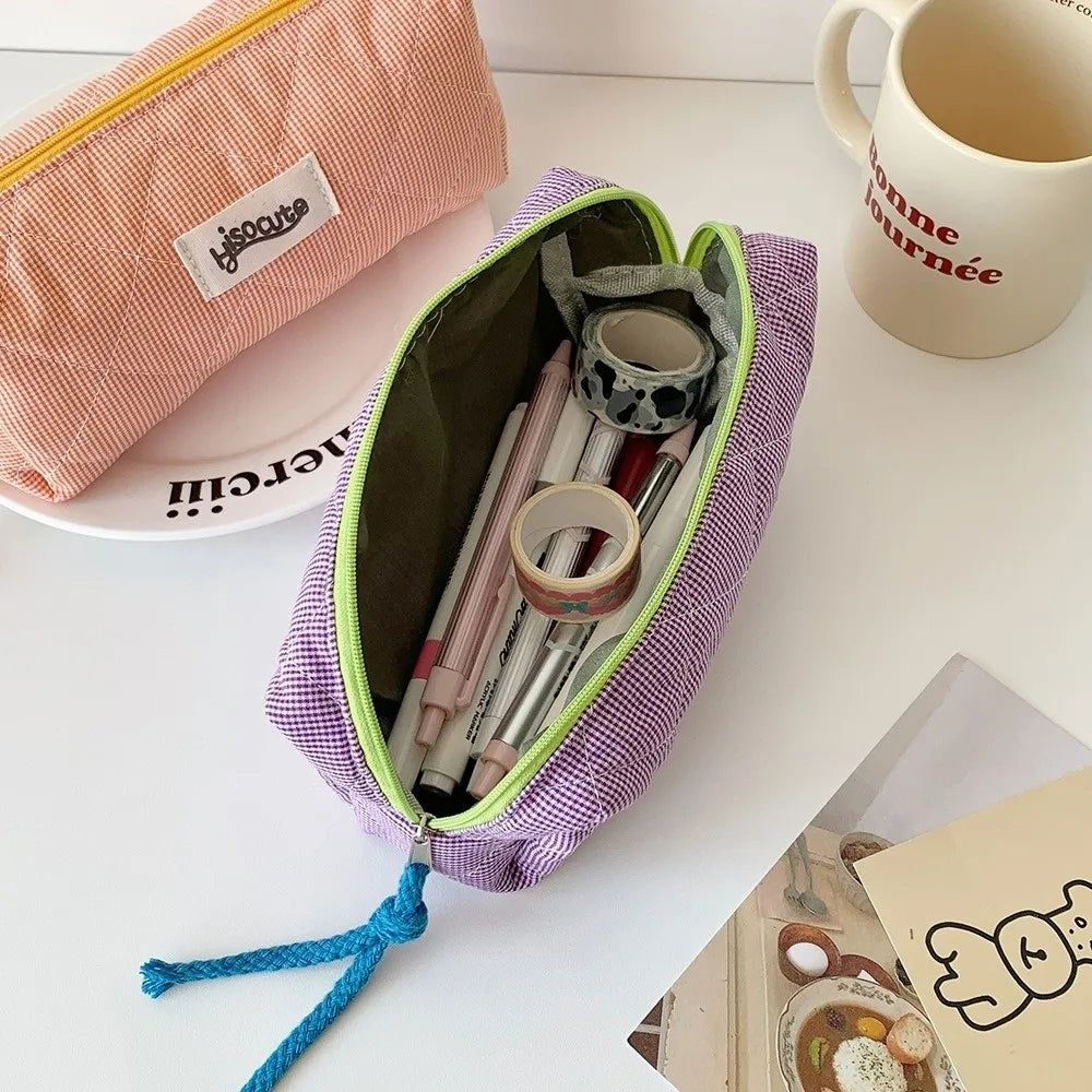 A purple checkered pencil case is open, showing various pens and pencils inside, resting on a white surface.
