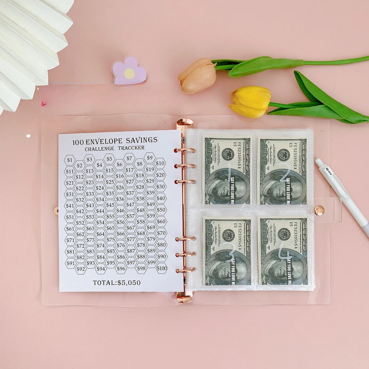 A pink A5 envelope budget binder set showing a challenge tracker and cash envelopes with US dollar bills.
