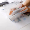 A hand holds a transparent storage book filled with various stickers and documents on a white surface.
