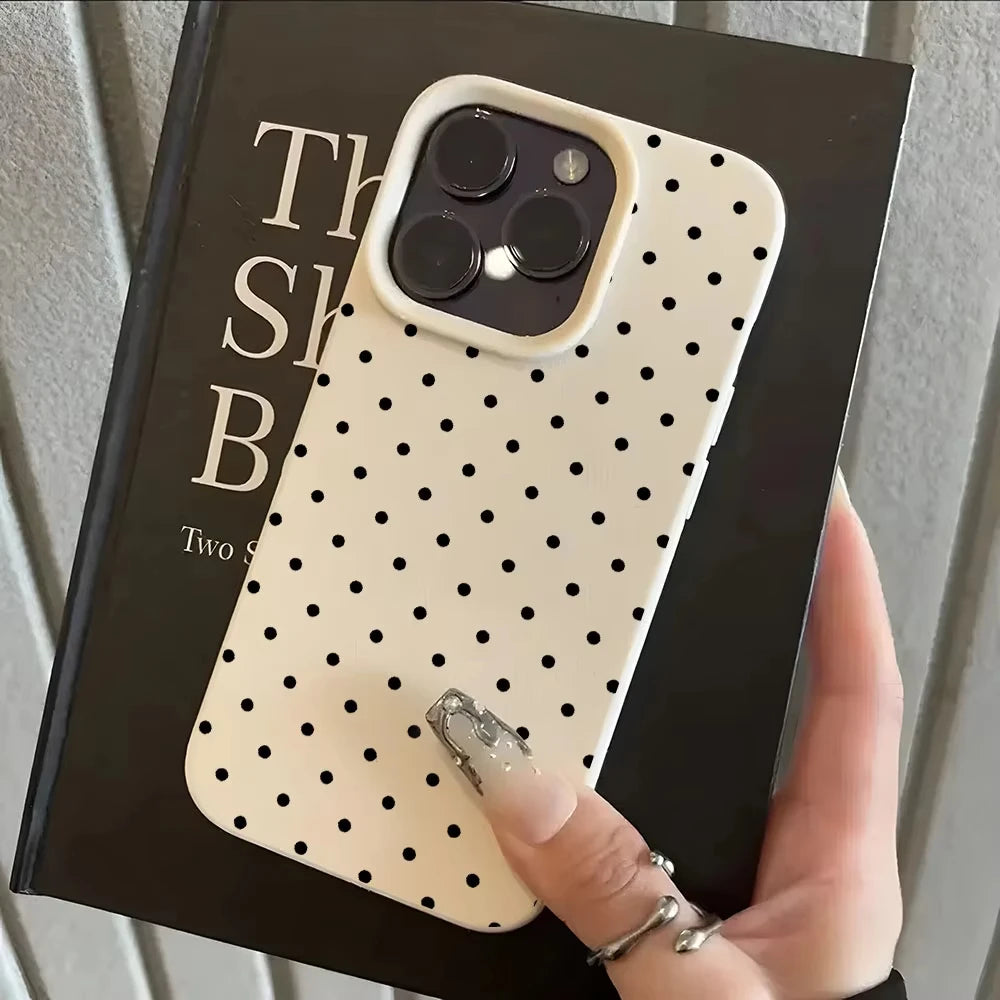 A hand holds a phone case with a light cream background and black polka dots, displayed against a dark box.