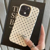 A hand holds a phone case with a light cream background and black polka dots, displayed against a dark box.