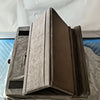 A gray foldable tablet pillow stand with a pocket is shown resting on a cardboard box inside clear plastic packaging.