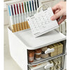 A white desk organizer with two clear storage drawers holds pens and a paper list.