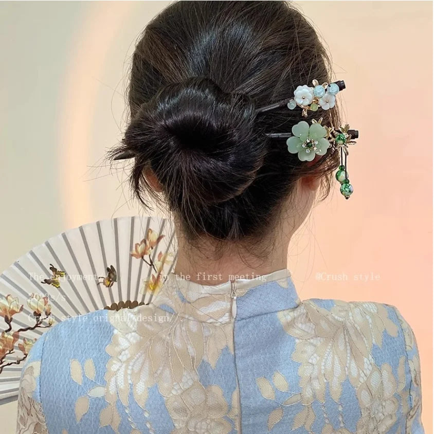 Les cheveux noirs d'une femme sont coiffés en chignon avec des accessoires floraux à fleurs blanches et vertes.
