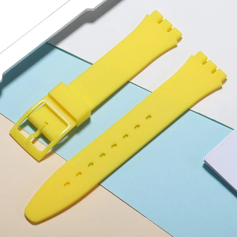 Yellow silicone watch strap with a buckle and replacement tools lying on blue and beige paper.