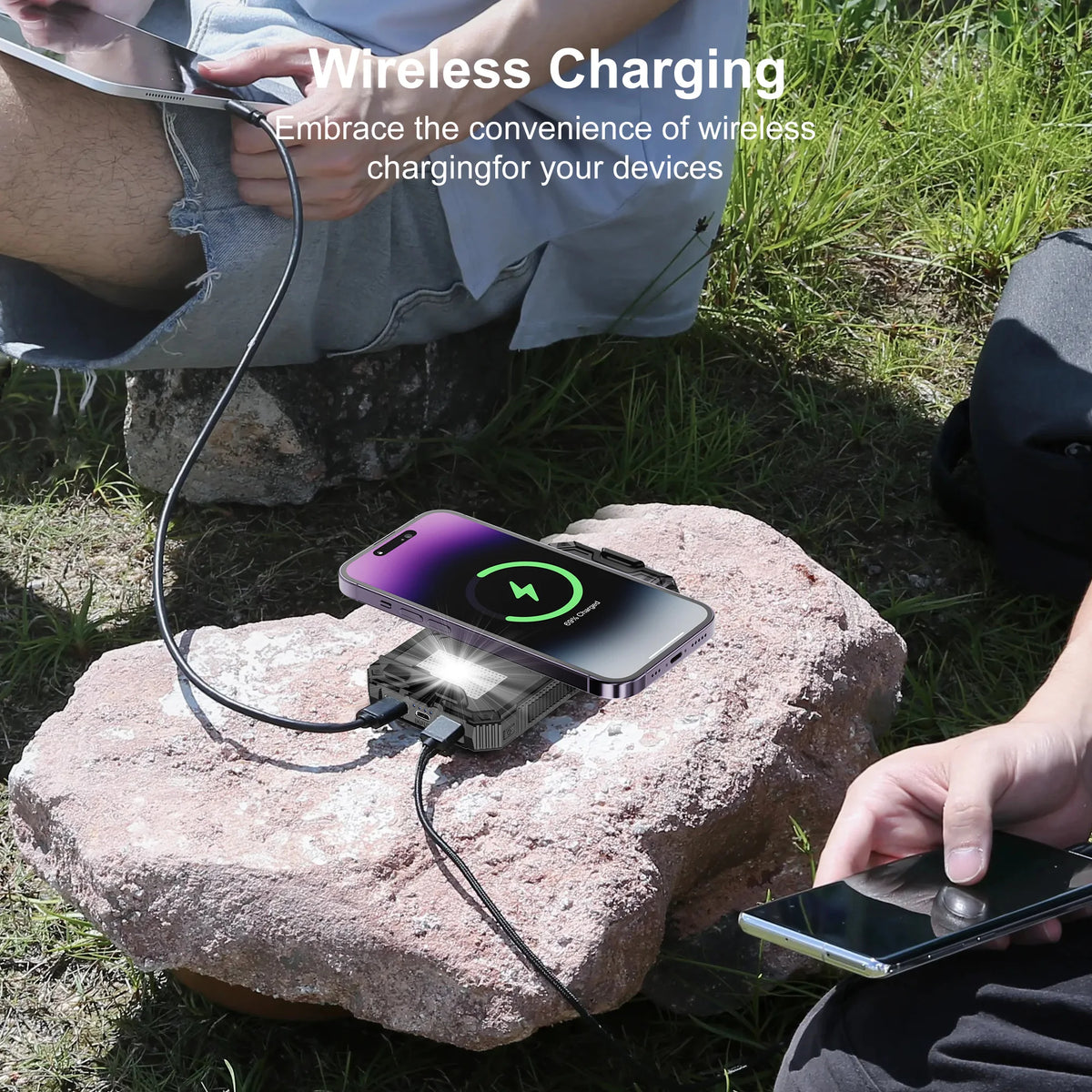 A hand is using a portable solar power bank charger to wirelessly charge a smartphone outdoors on a rock.