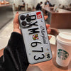 A hand holds a silver vintage license plate phone case for an iPhone with Maryland text and a green Starbucks cup in the back