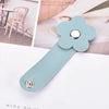 A light blue leather flower cable organizer with a silver button, shown next to a wooden chair and greenery.