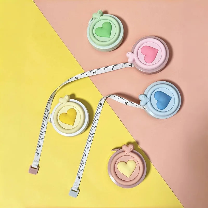 Cinta métrica retráctil en forma de corazón con cinta y marcas de medición de varios colores sobre un fondo rosa y amarillo