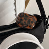 A glossy tortoiseshell protective case for AirPods is placed inside a black bag.