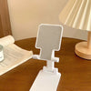A white adjustable foldable phone and tablet stand resting on a wooden table next to an open book.