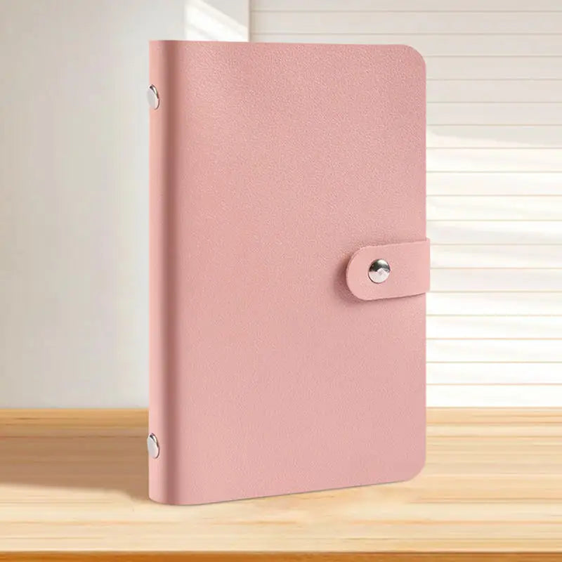 A pink reusable binder with a cover and a silver clasp resting on a wooden surface.