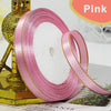 Pink gold edge satin ribbon rolled on a stand with green foliage in the background