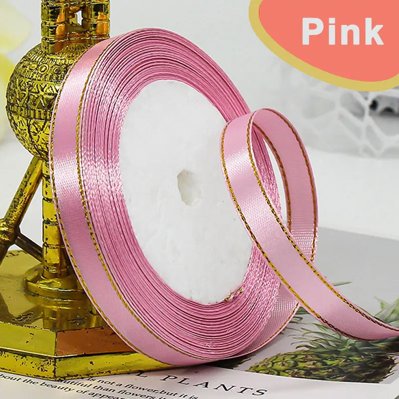 Pink gold edge satin ribbon rolled on a stand with green foliage in the background
