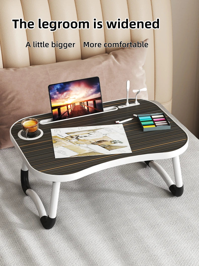 A wooden laptop desk organizer tray with a laptop, pens, and colored pencils placed on it.