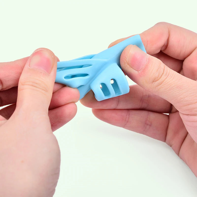 A hand holds a light blue silicone pencil grip writing corrector for children.