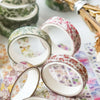 A collection of five rolls of floral patterned washi tape for crafting and journaling displayed on a white surface.