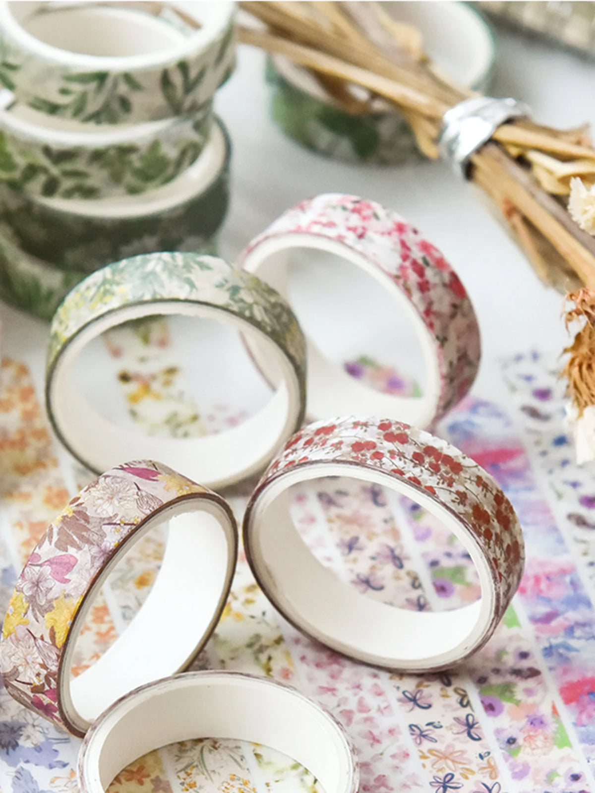 A collection of five rolls of floral patterned washi tape for crafting and journaling displayed on a white surface.