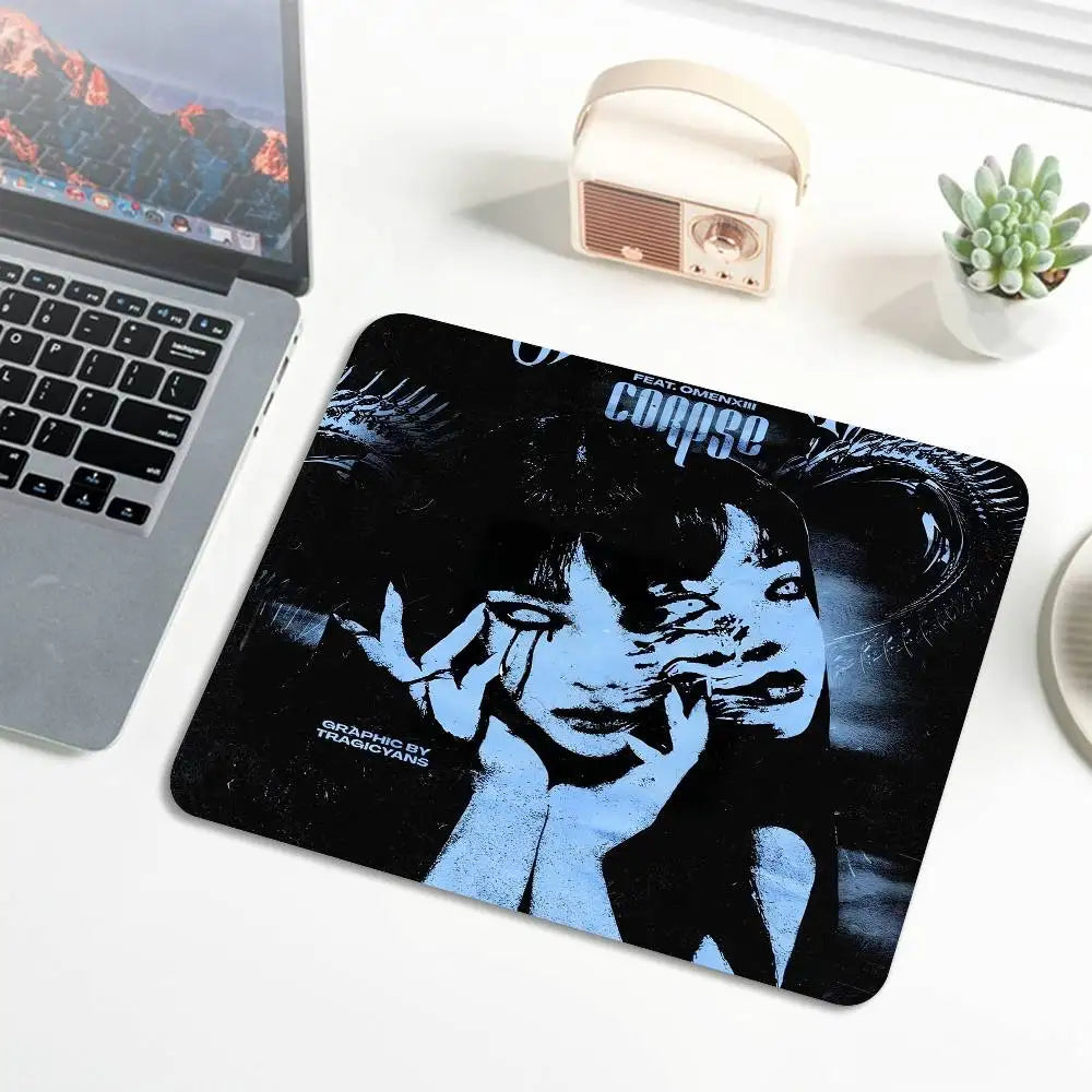 A black mouse pad featuring a blue and black graphic of Tomie from Junji Ito, with stitched edges, placed next to a laptop an