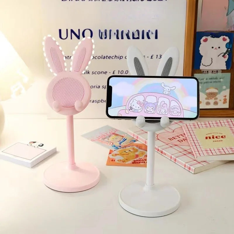 A pink rabbit mobile phone stand with a white base and a smartphone displayed on it.