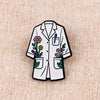 Enamel pin of a white lab coat featuring floral embroidery and a pencil detail.