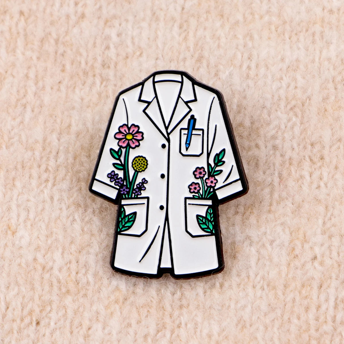 Enamel pin of a white lab coat featuring floral embroidery and a pencil detail.