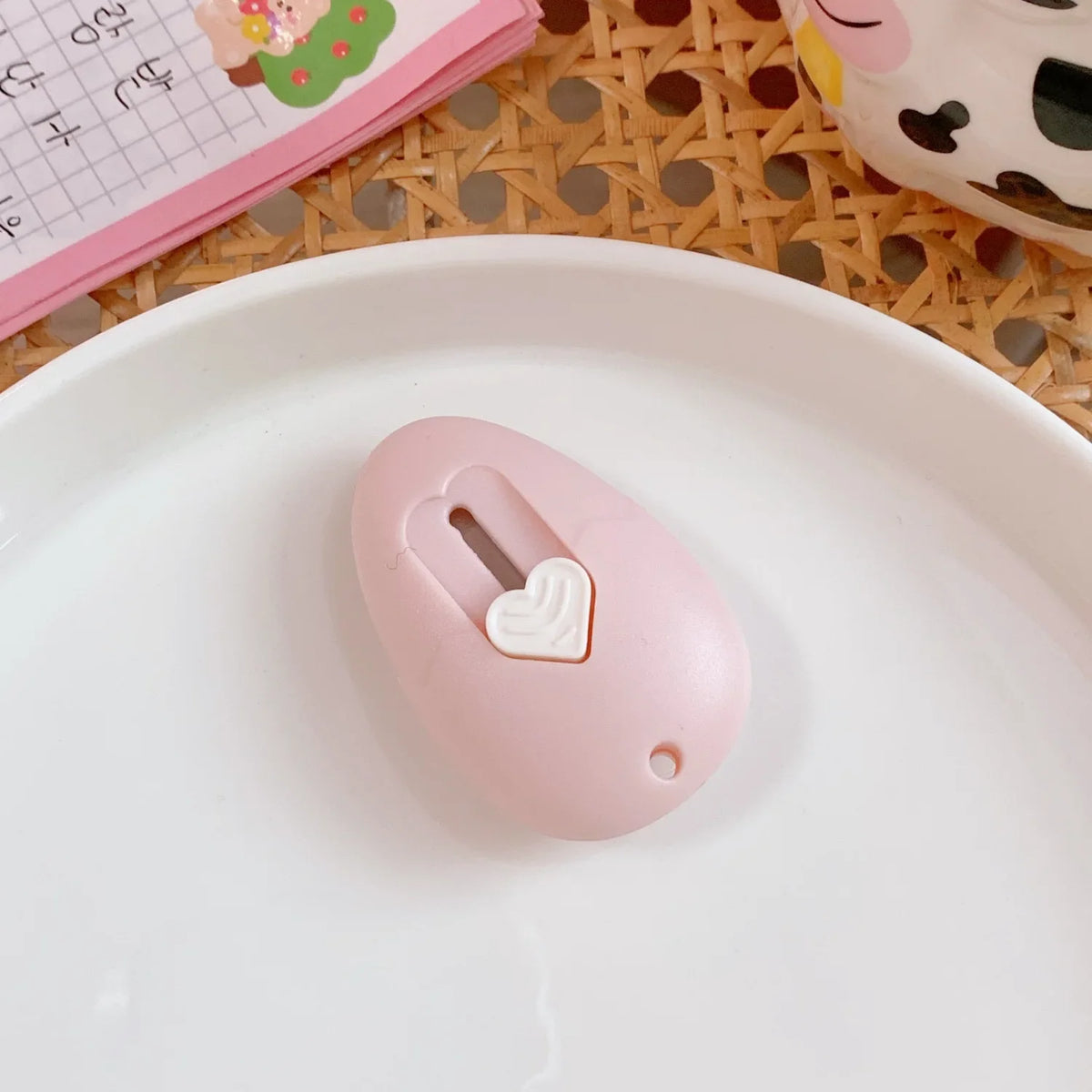 A pink cat paw mini cutter is placed on a white plate next to a notebook and woven mat.