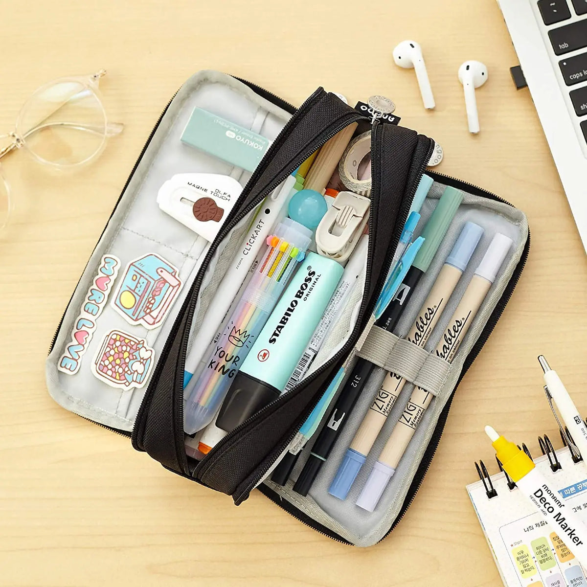 A black fabric pencil pouch organizer filled with various pens, pencils, and a white eraser on a wooden surface.