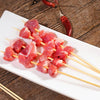 A plate of raw red meat cubes skewered on bamboo sticks with chili peppers in the background.