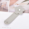 A gray leather flower cable organizer with a silver stud, shown next to a blurred background of wooden furniture.